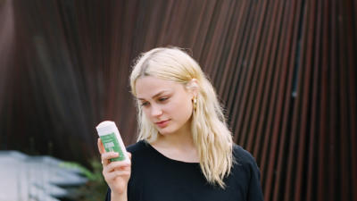 Woman holding schmidt's jasmine tea deodorant and looking down at it